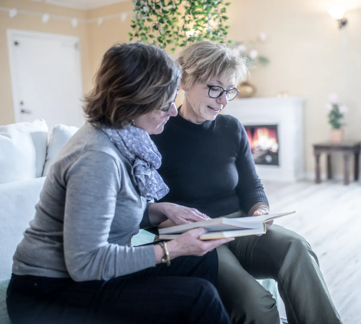 Two older women reading a book together at home