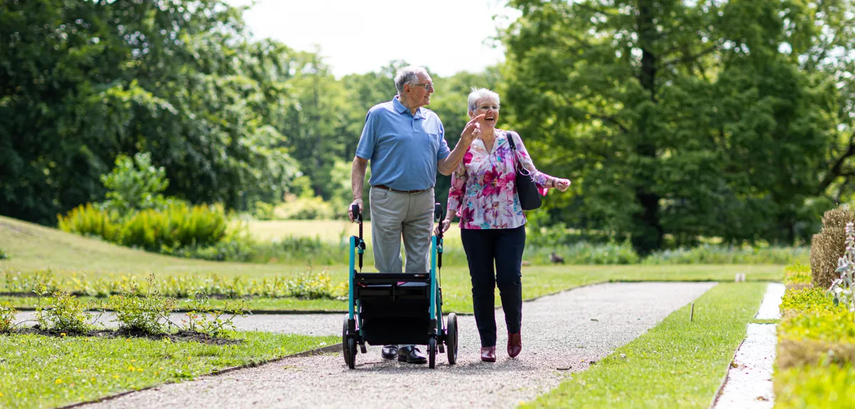 Older adults walking on a park path with a rollator