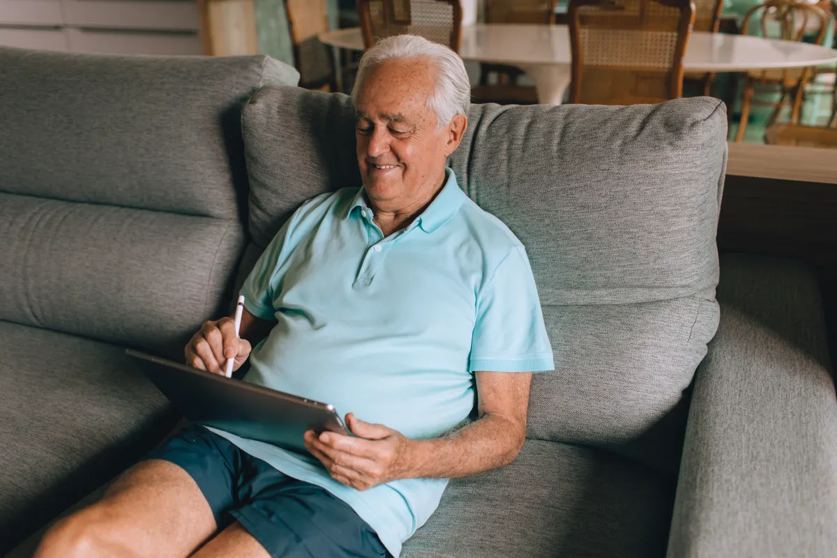 Older man using a tablet while sitting on a sofa