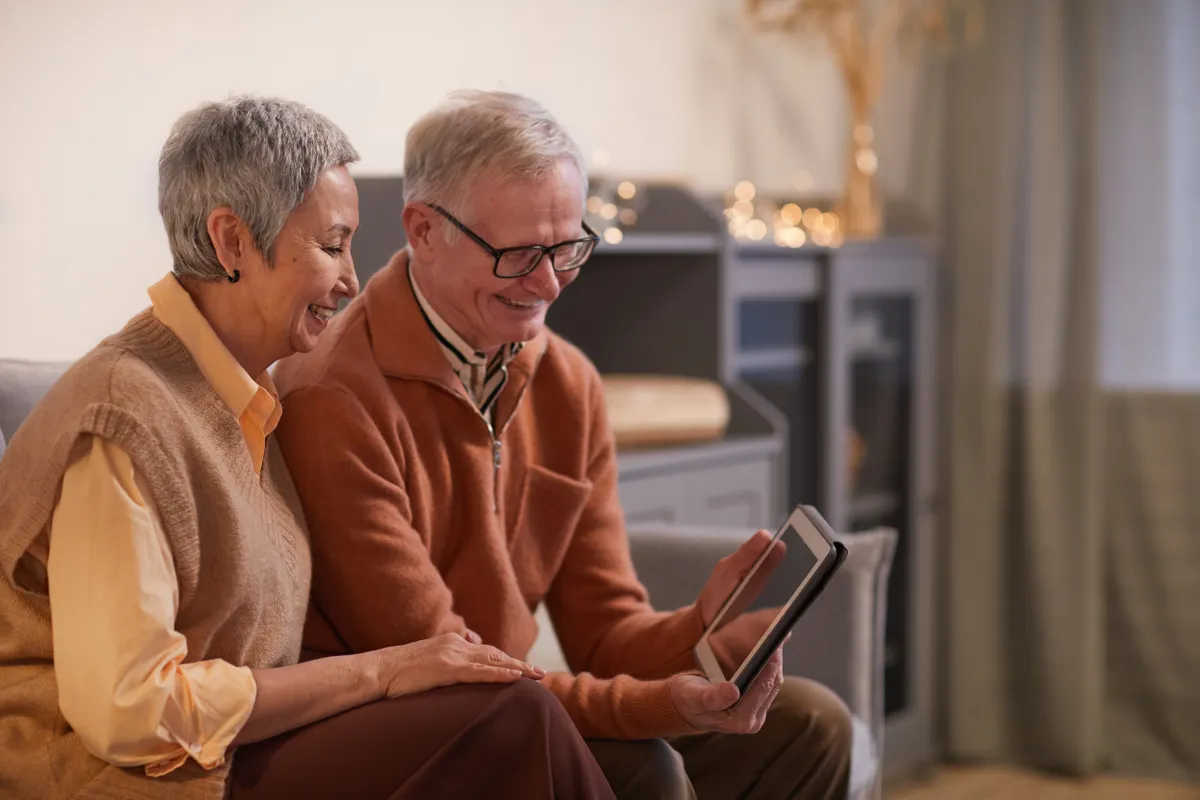Older couple smiling while looking at a tablet