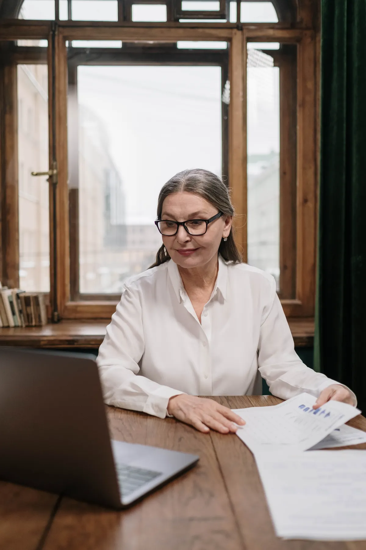 Older woman reviewing papers beside a laptop