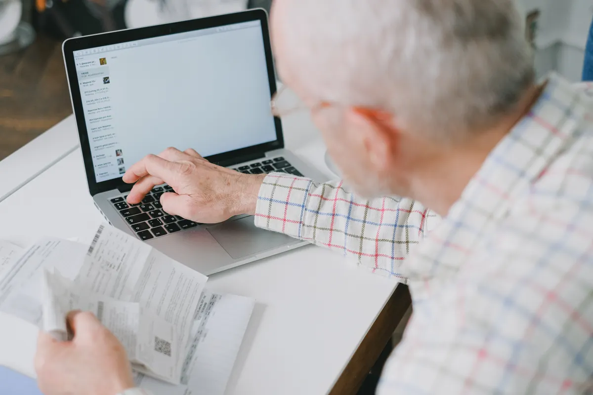Older man using a laptop alongside printed documents