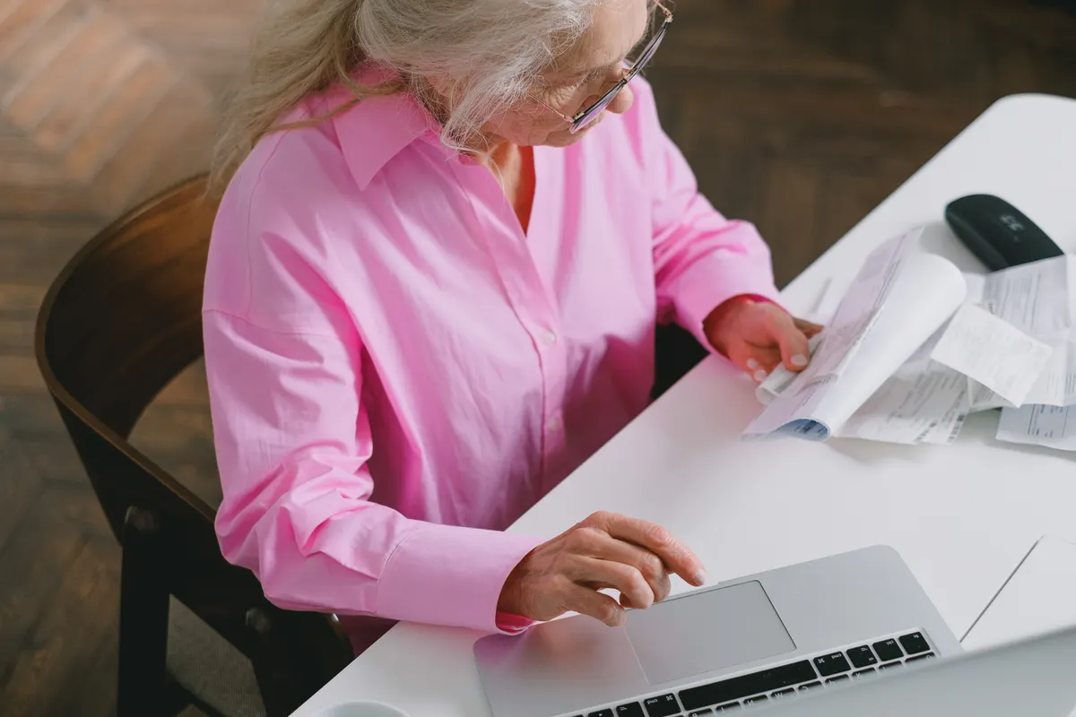 Older woman checking documents while using a laptop