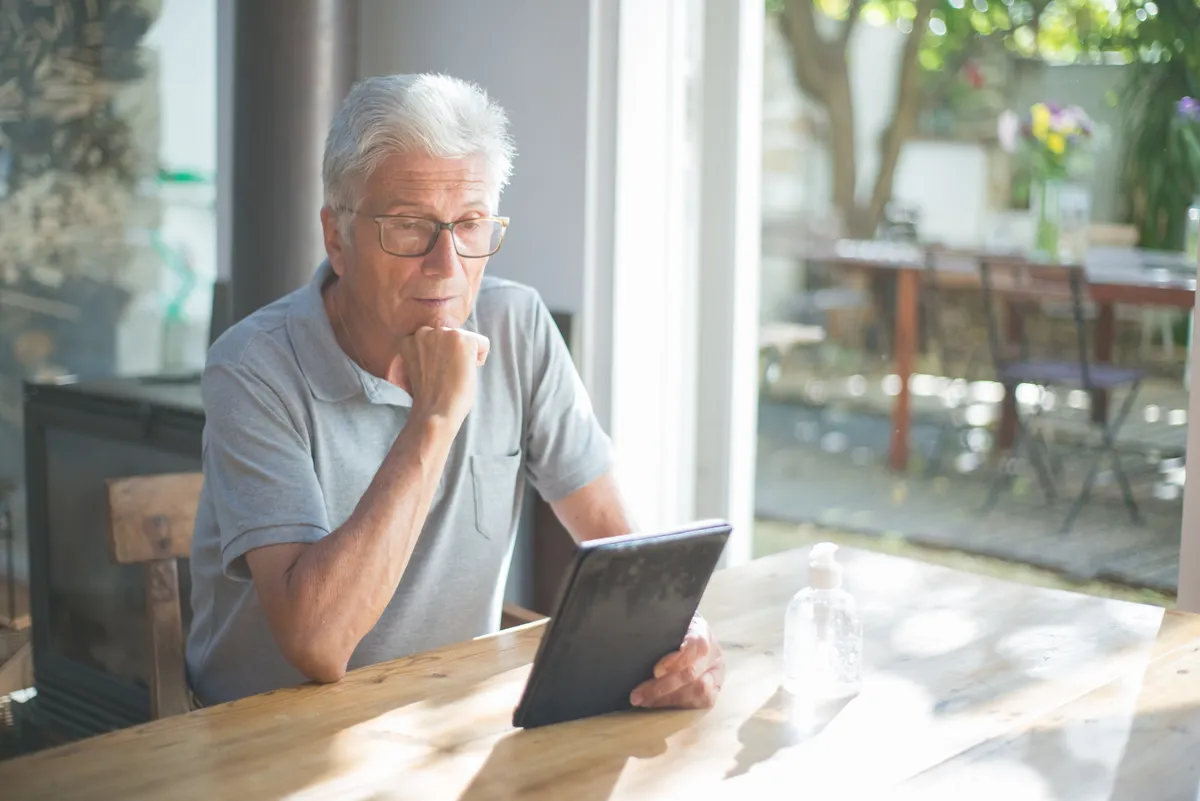 Older man reading a tablet beside a sunny window