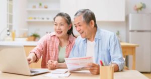 An older couple reviewing Medicare plans on a laptop, with documents and a coffee cup on the table.