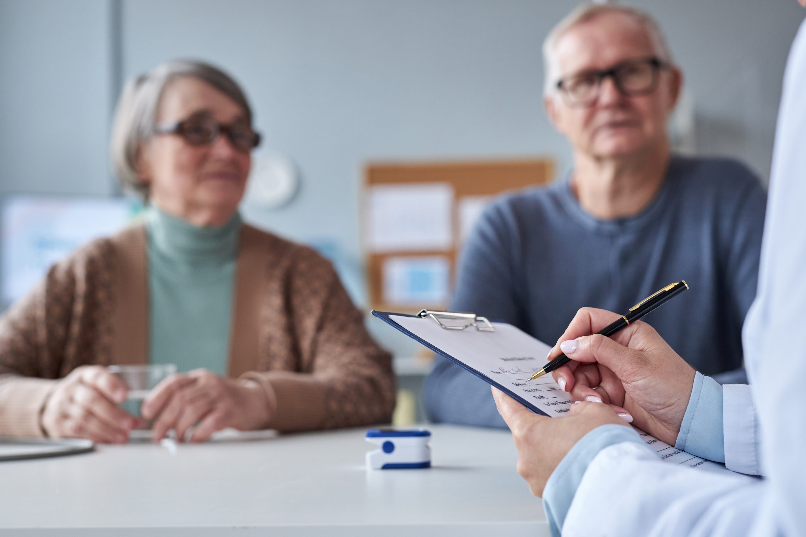 A senior couple attentively listening to a healthcare professional in a medical office, discussing treatment options and lifestyle changes.

