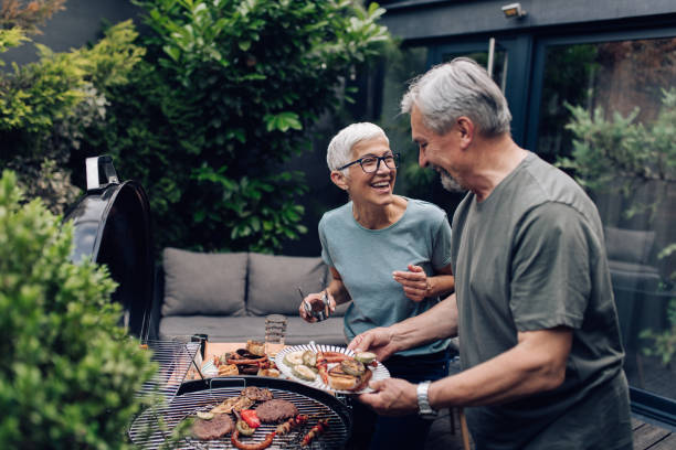 Smiling senior couple grilling food outdoors, enjoying a meal together, symbolizing the benefits of long-term care insurance in maintaining quality of life.