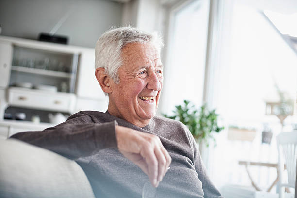 Smiling elderly man sitting in a bright, cozy living room, representing a satisfied Medicare Supplement Insurance beneficiary