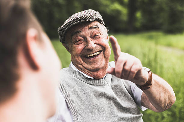 An elderly man wearing a cap and smiling while giving a thumbs-up outdoors, symbolizing improved quality of life and well-being.