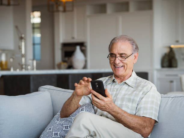 Smiling elderly man sitting in a modern living room, using his smartphone, representing confidence in managing Medicare Plan F costs