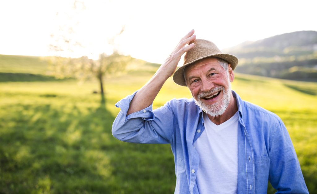 A cheerful elderly man outdoors, tipping his hat with a smile, representing confidence and ease in navigating healthcare processes.