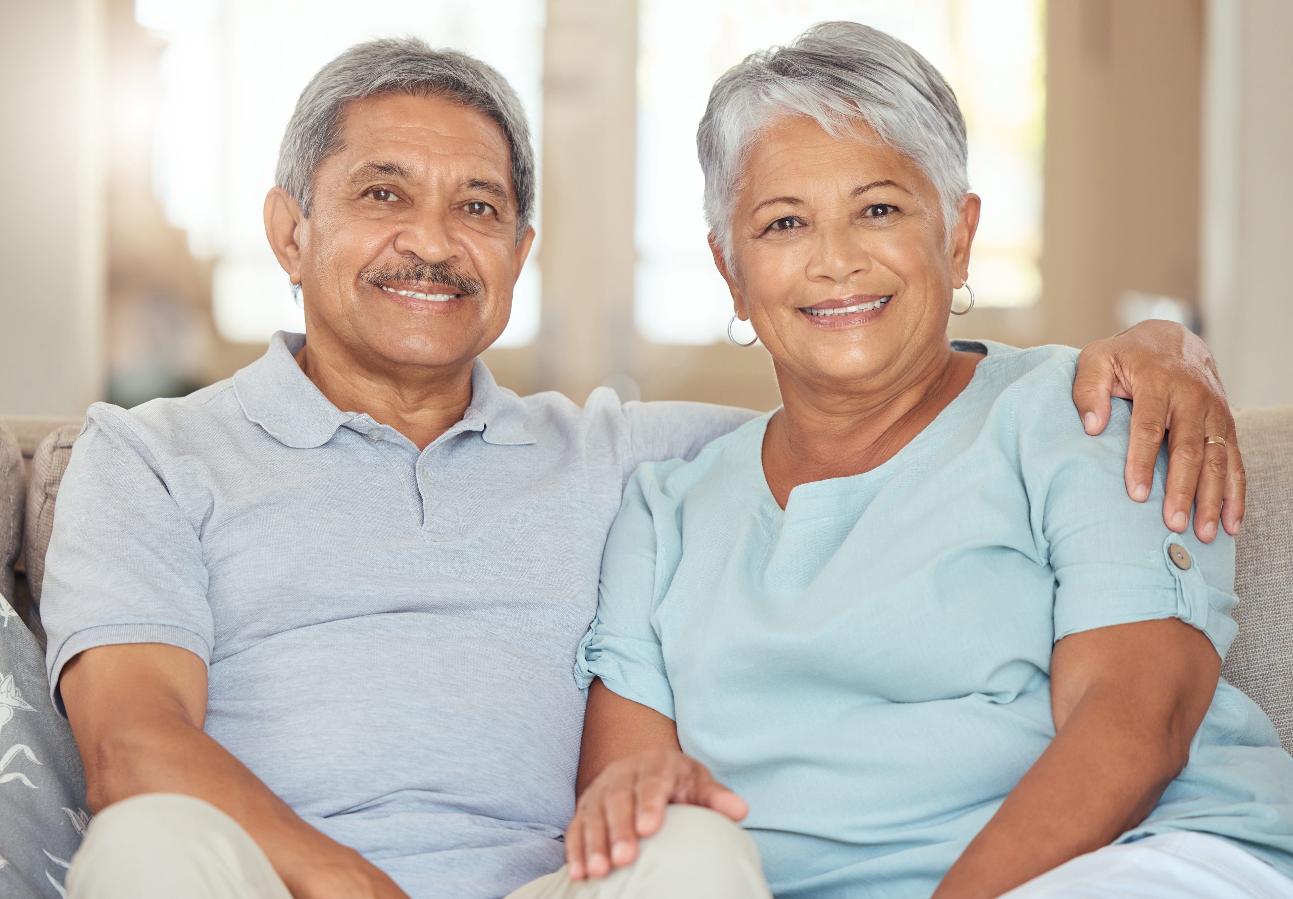 A smiling senior couple sitting together on a couch in a well-lit living room, looking confident and reassured.