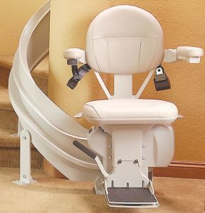 A stair lift with a beige cushioned seat and curved rail installed on a wooden staircase, designed to assist with mobility in homes.