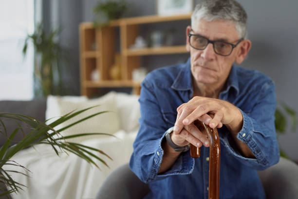 An elderly man sitting and resting his hands on a wooden walking cane, reflecting the importance of Medicaid coverage for mobility aids.

