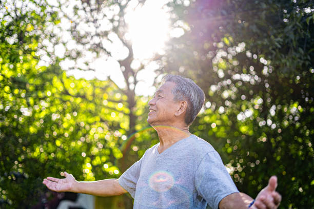 "Older man standing outdoors with open arms, enjoying the sunlight, symbolizing health and well-being." 